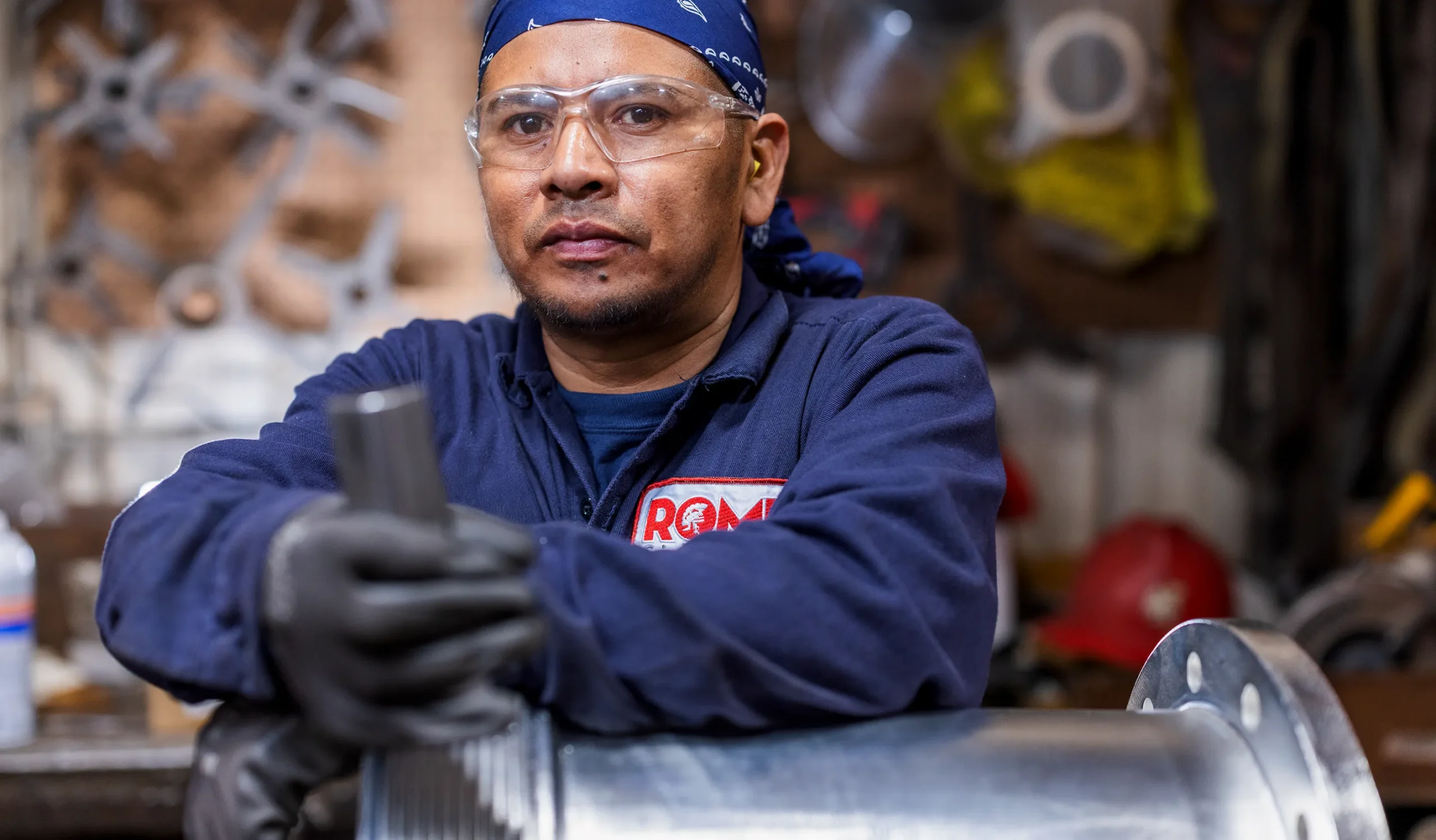 Man in blue working kit rome logo on lean over a machine face to camera