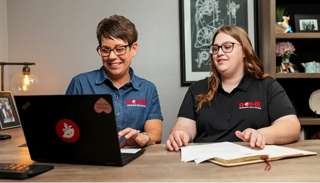 Resources Rome Grinding two women on table looking on laptop